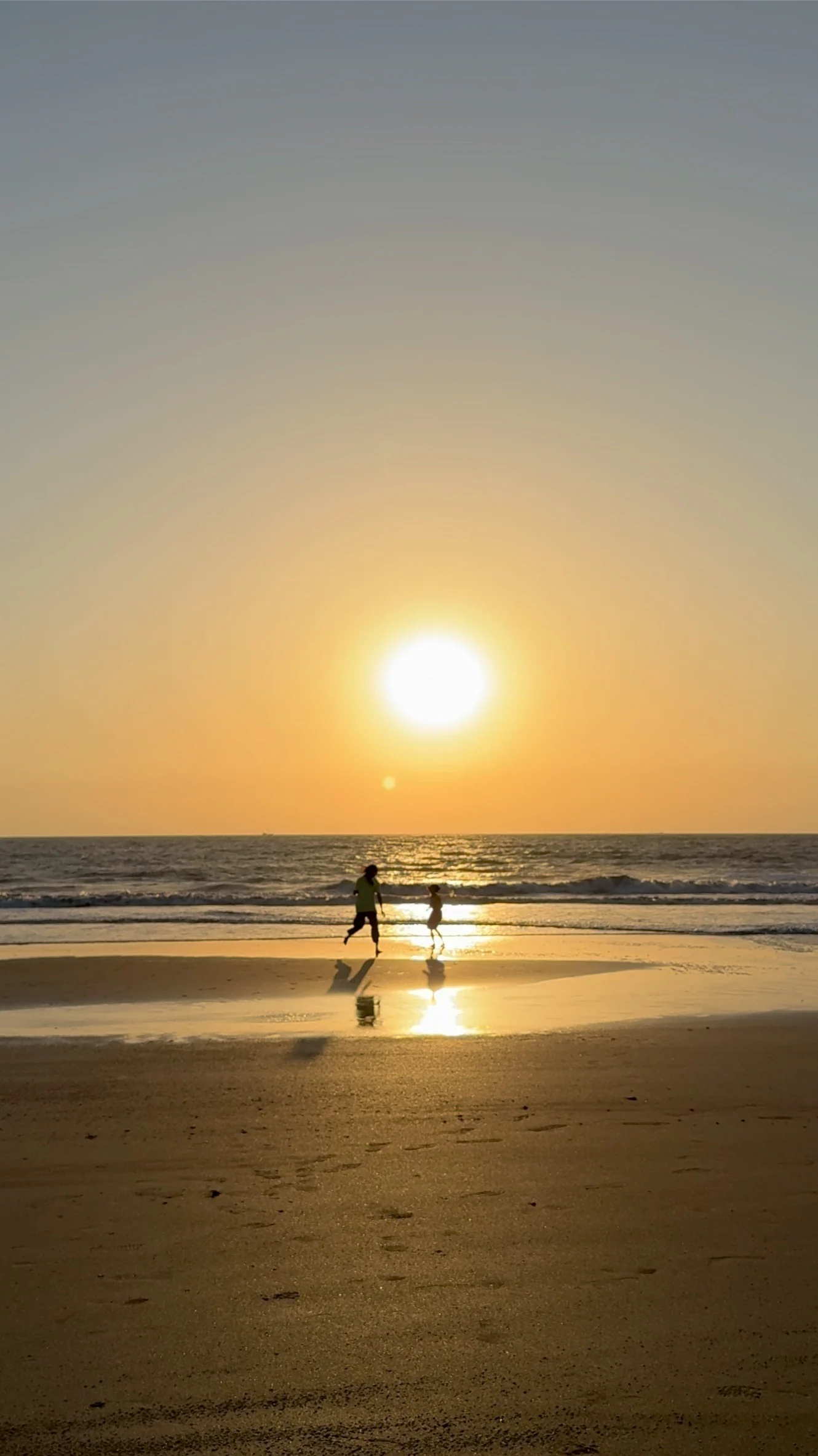 Two silhouetted figures running along the shoreline at sunset