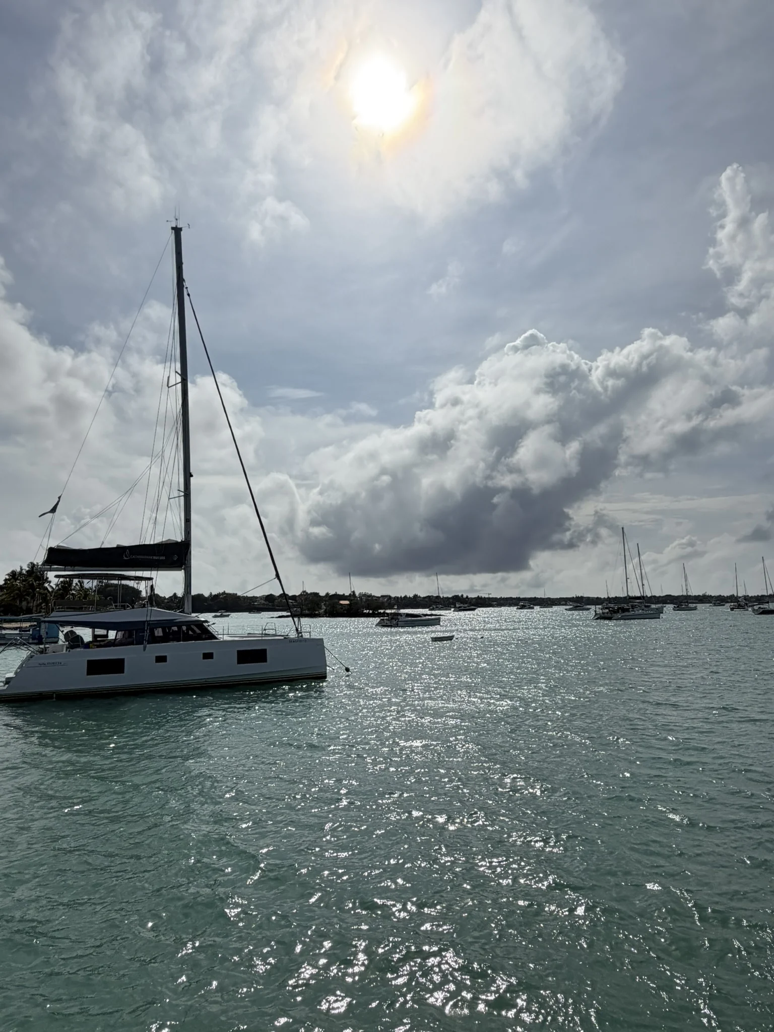 A moored catamaran beneath sunlit clouds on a calm bay